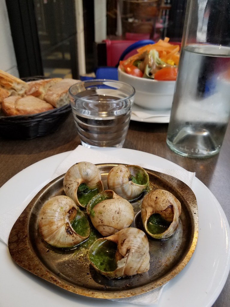 Plate of escargot with cup of water and bread on a table cafe in Paris