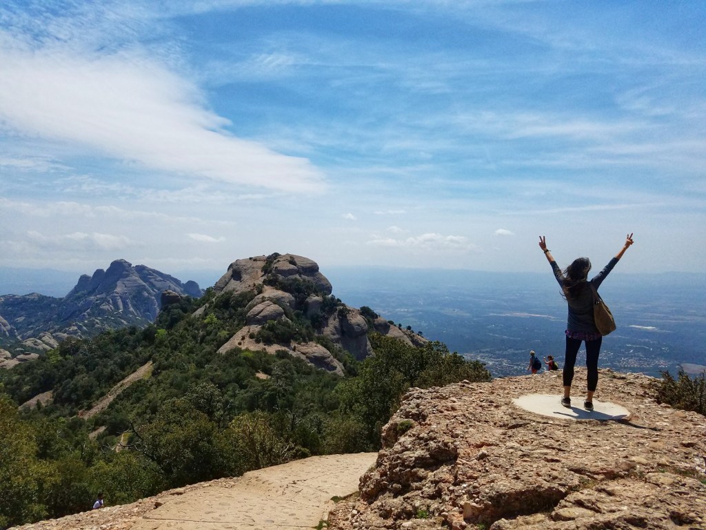 Women with hands raised looking out over a valley in Montserrat Spain
