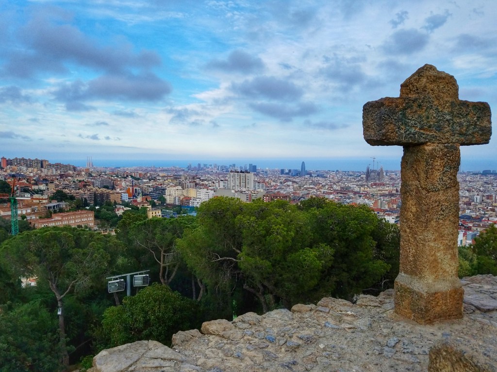 Stone cross statue in Park Guell overlooking the city of Barcelona Spain