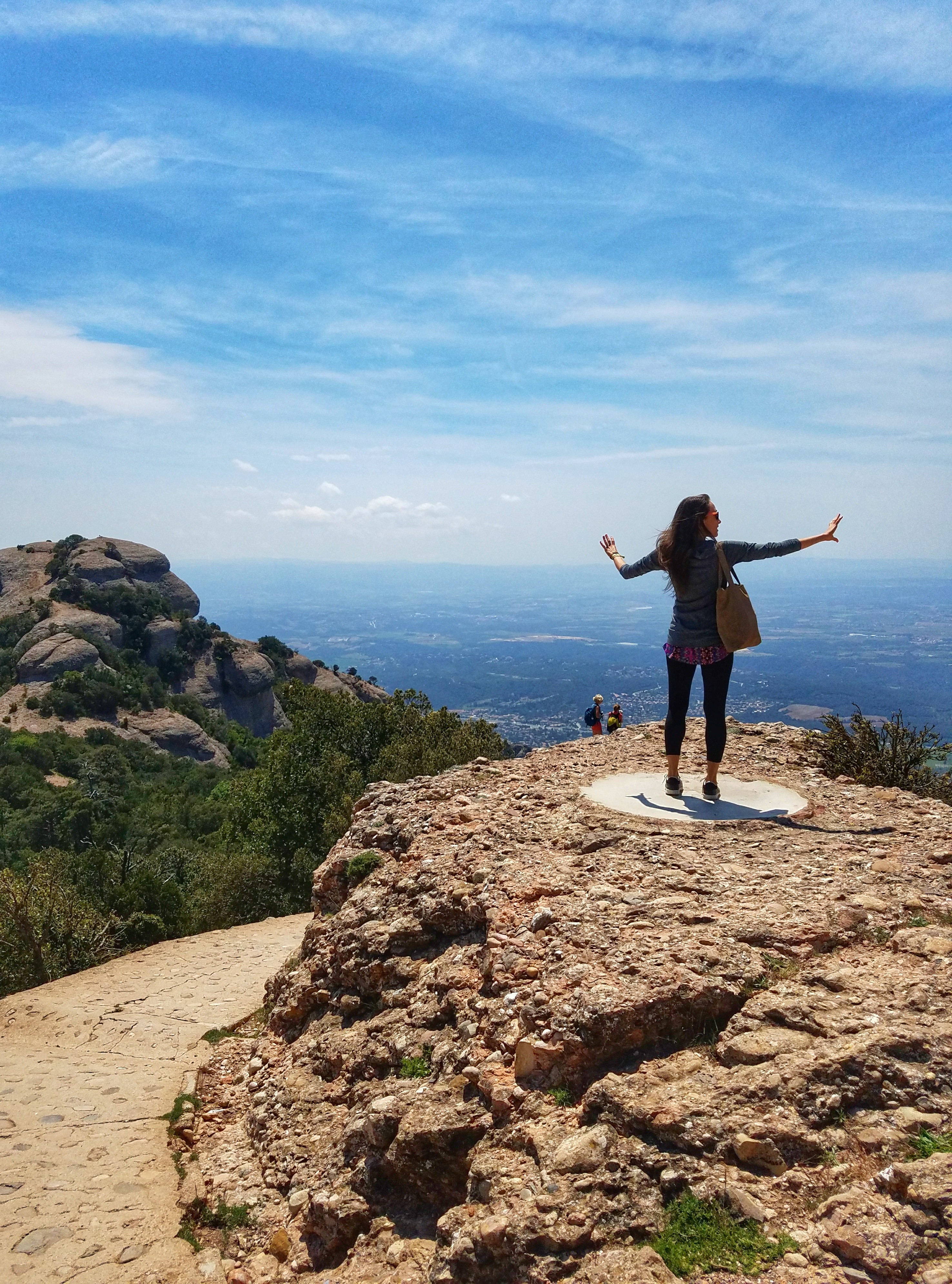 Woman standing near the edge of a cliff with hands outstretched and valley below