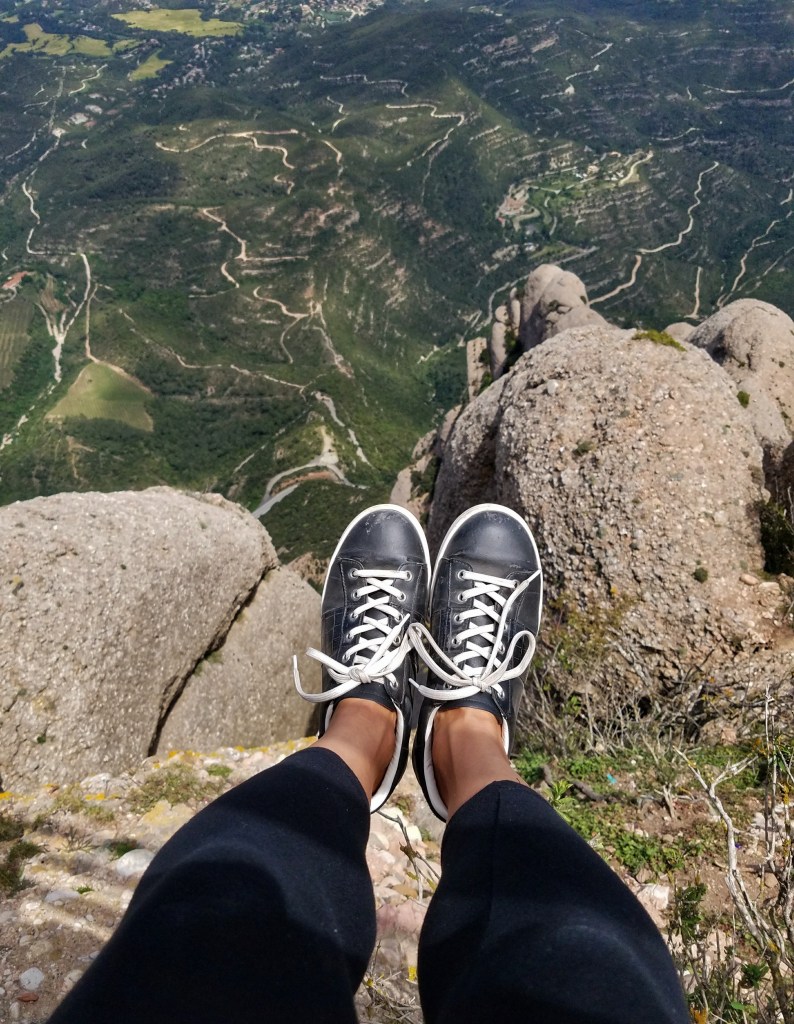 Feet dangling above a valley with black and white tennis shoes