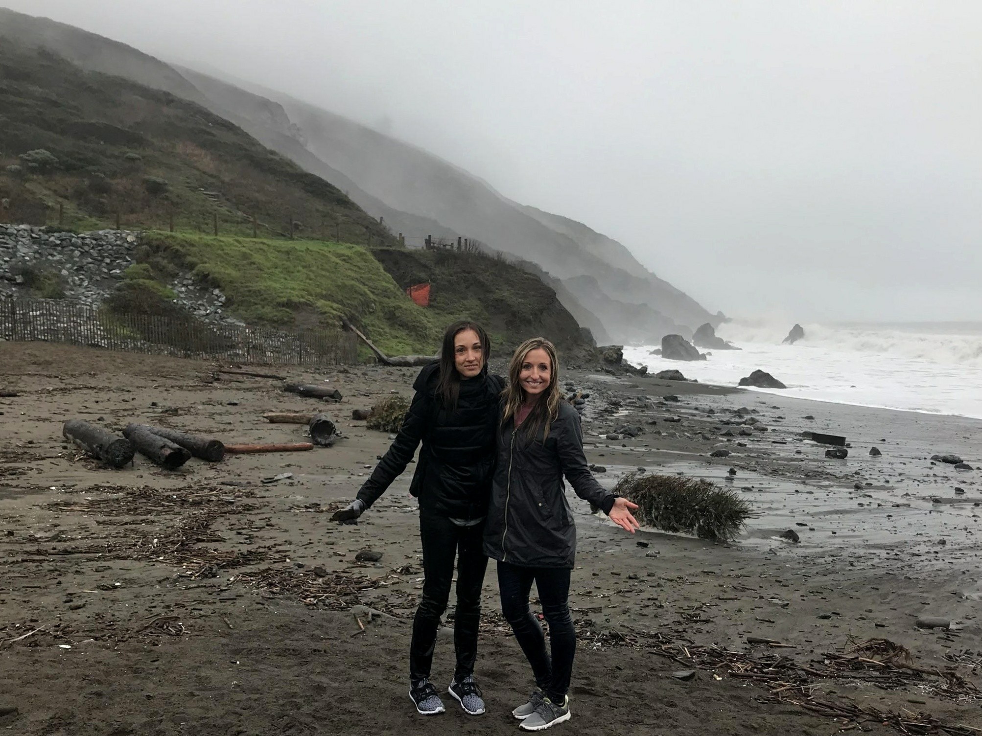 Two women posing in front of the Pacific Ocean cost