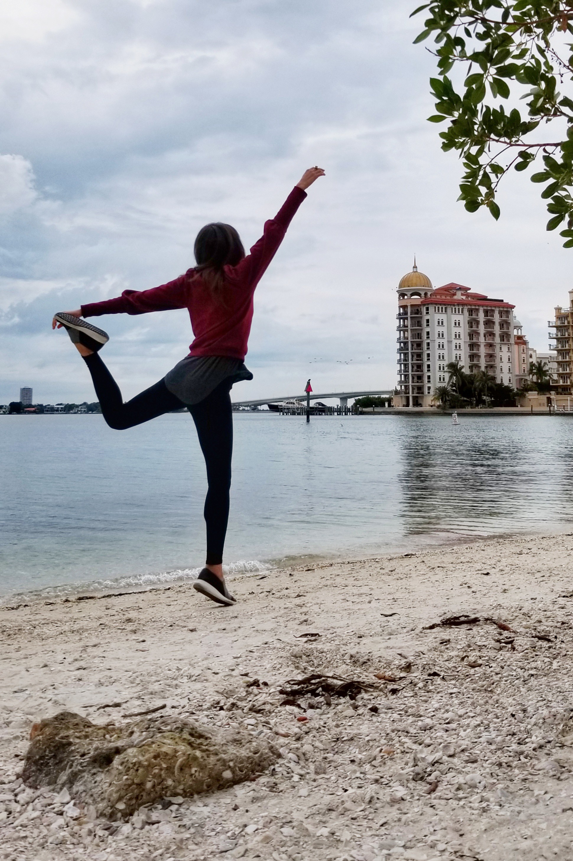 Woman dancing on a beach with a condo and causeway in view