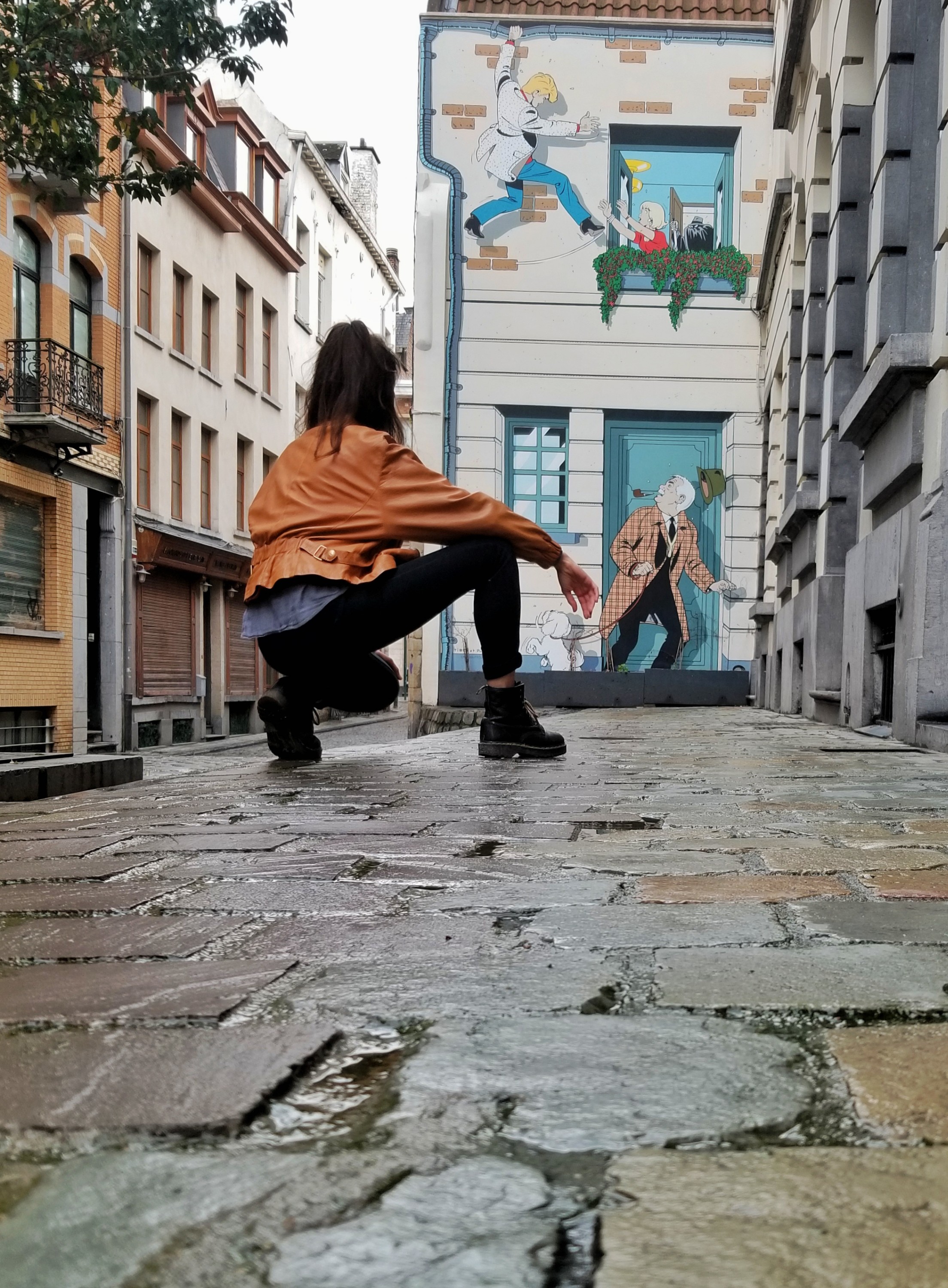 Woman kneeling on a sidewalk in front of a mural