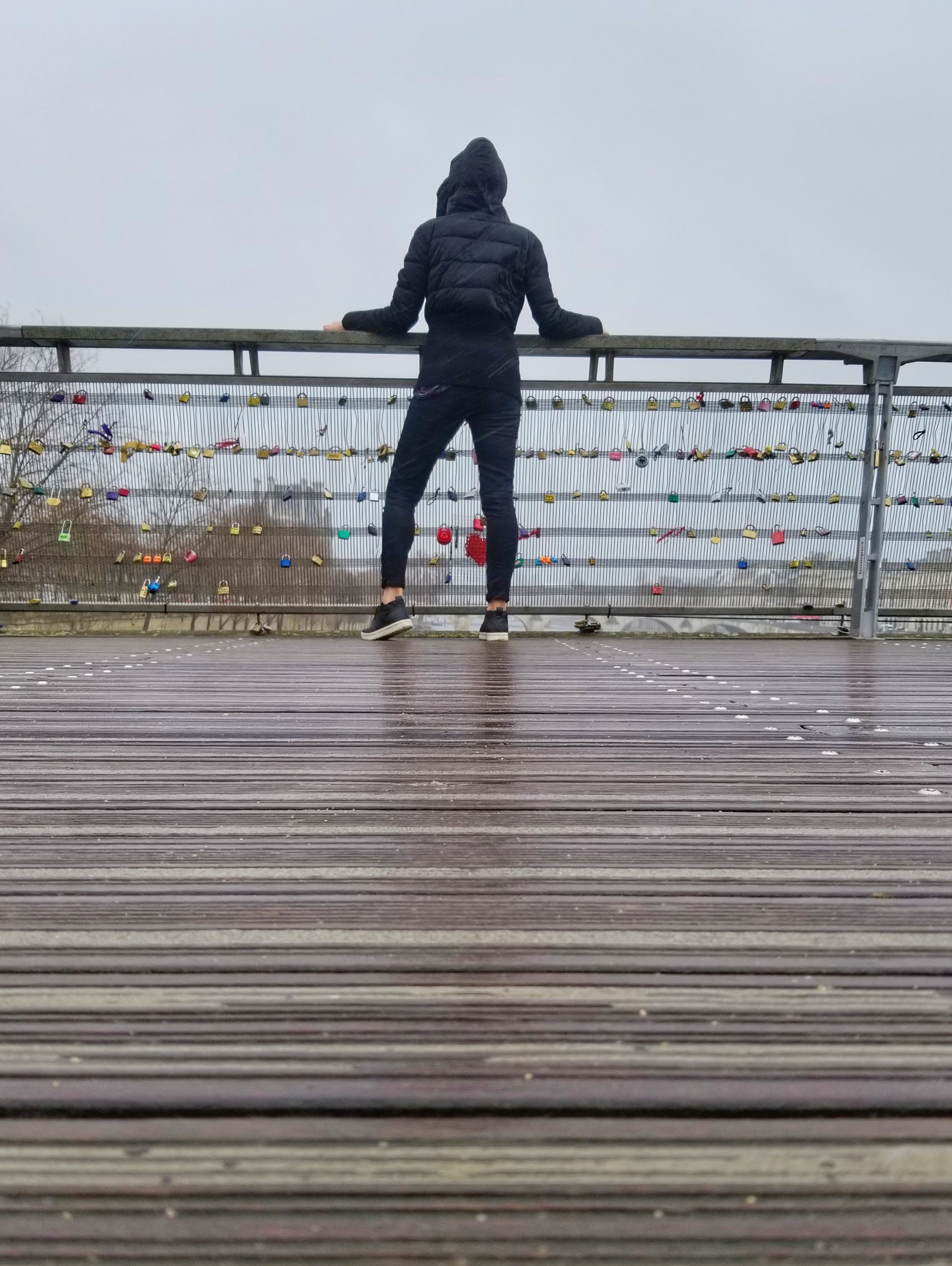 Person in all black standing at the railing of a love locks bridge