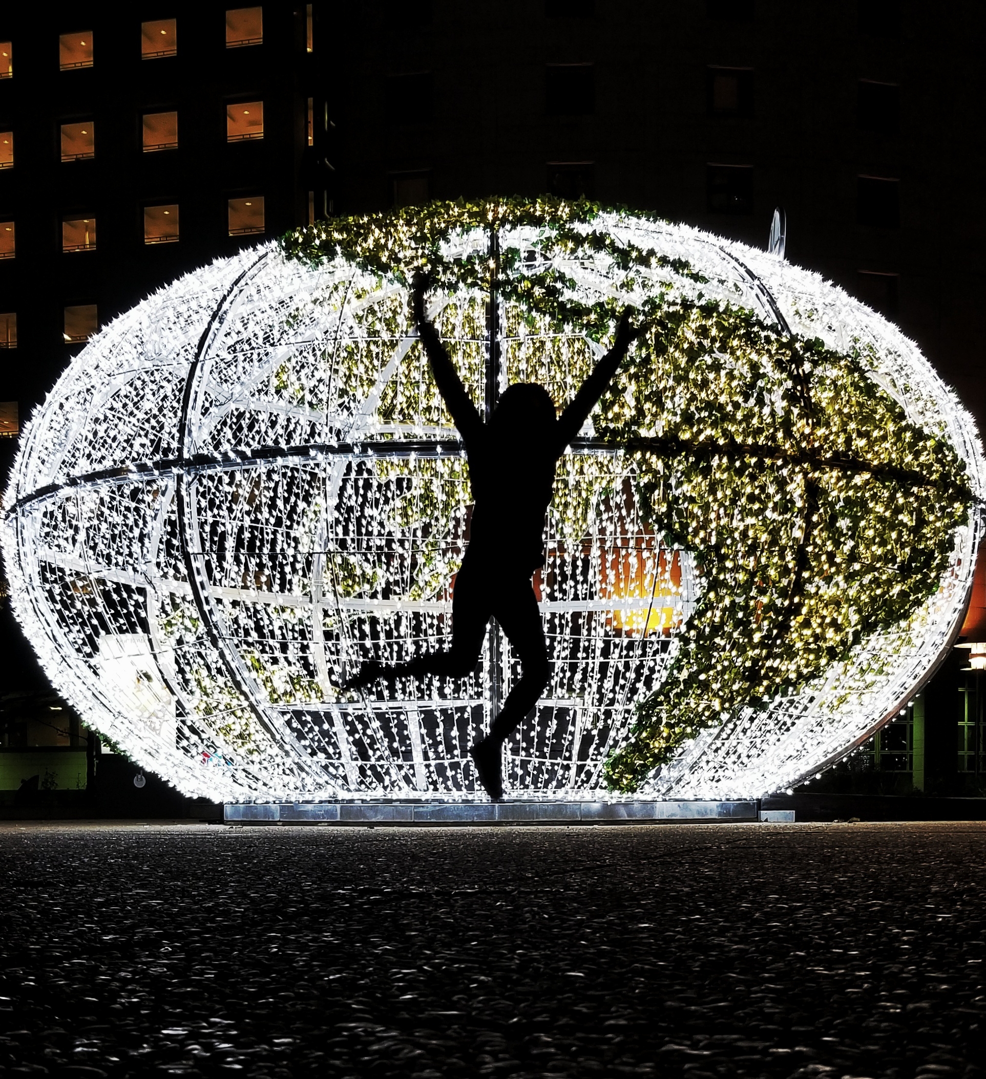 Silhouette s person jumping in front of a giant, lighted globe 