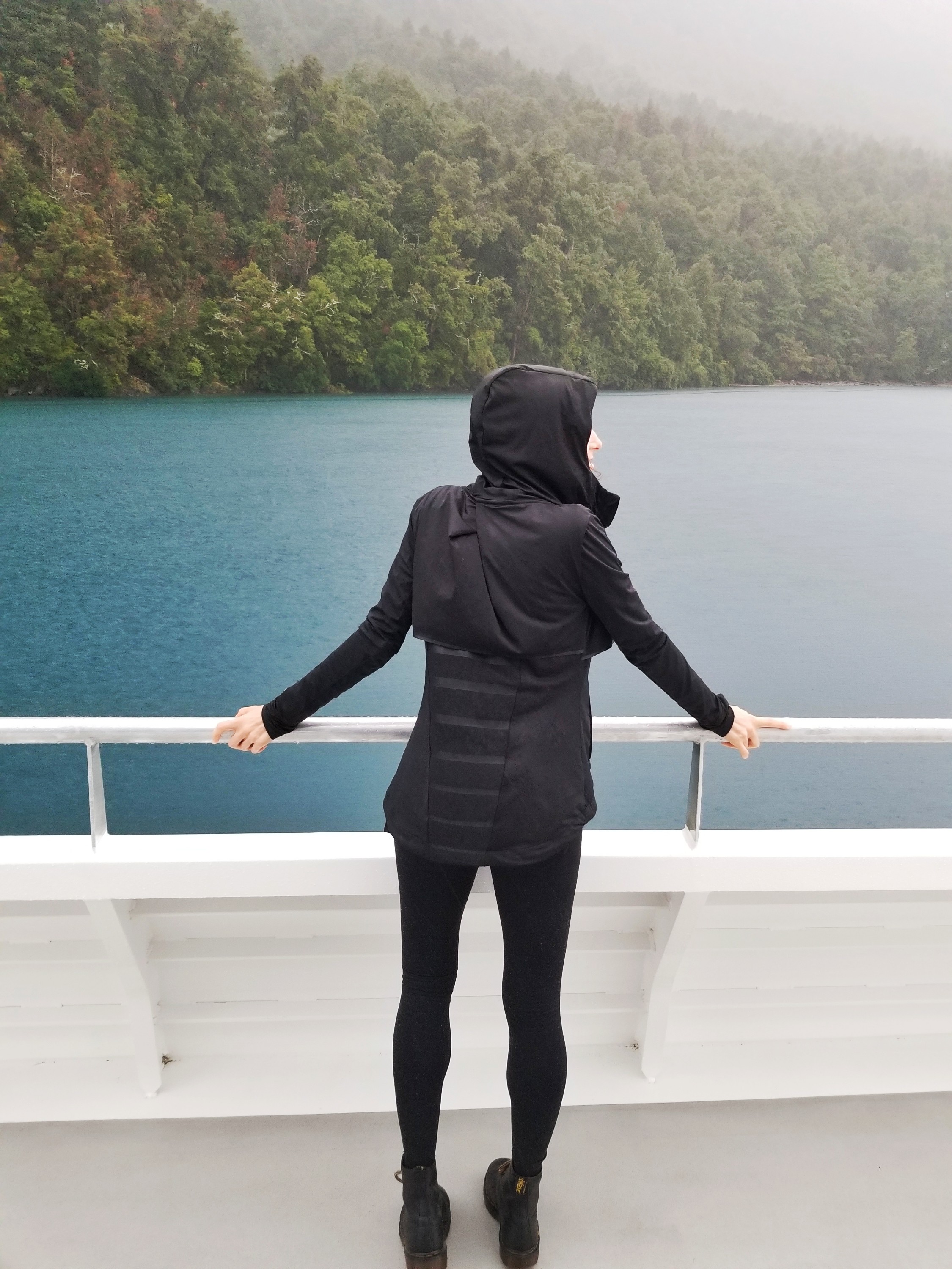 Person in a black coat standing at the guard rail of a boat