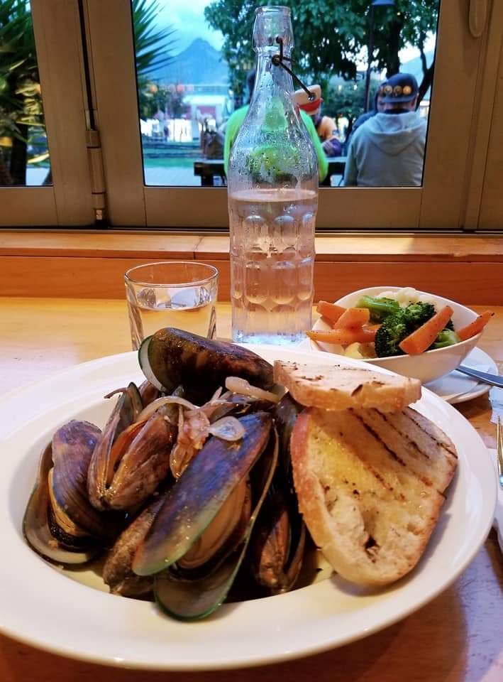 Plate of green-lipped mussels and toasted bread with a bowl of vegetables  and cup of water