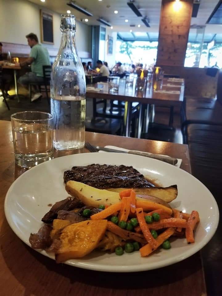 Grilled kangaroo, potatoes, and vegetables on a plate with a glass of water in a restaurant