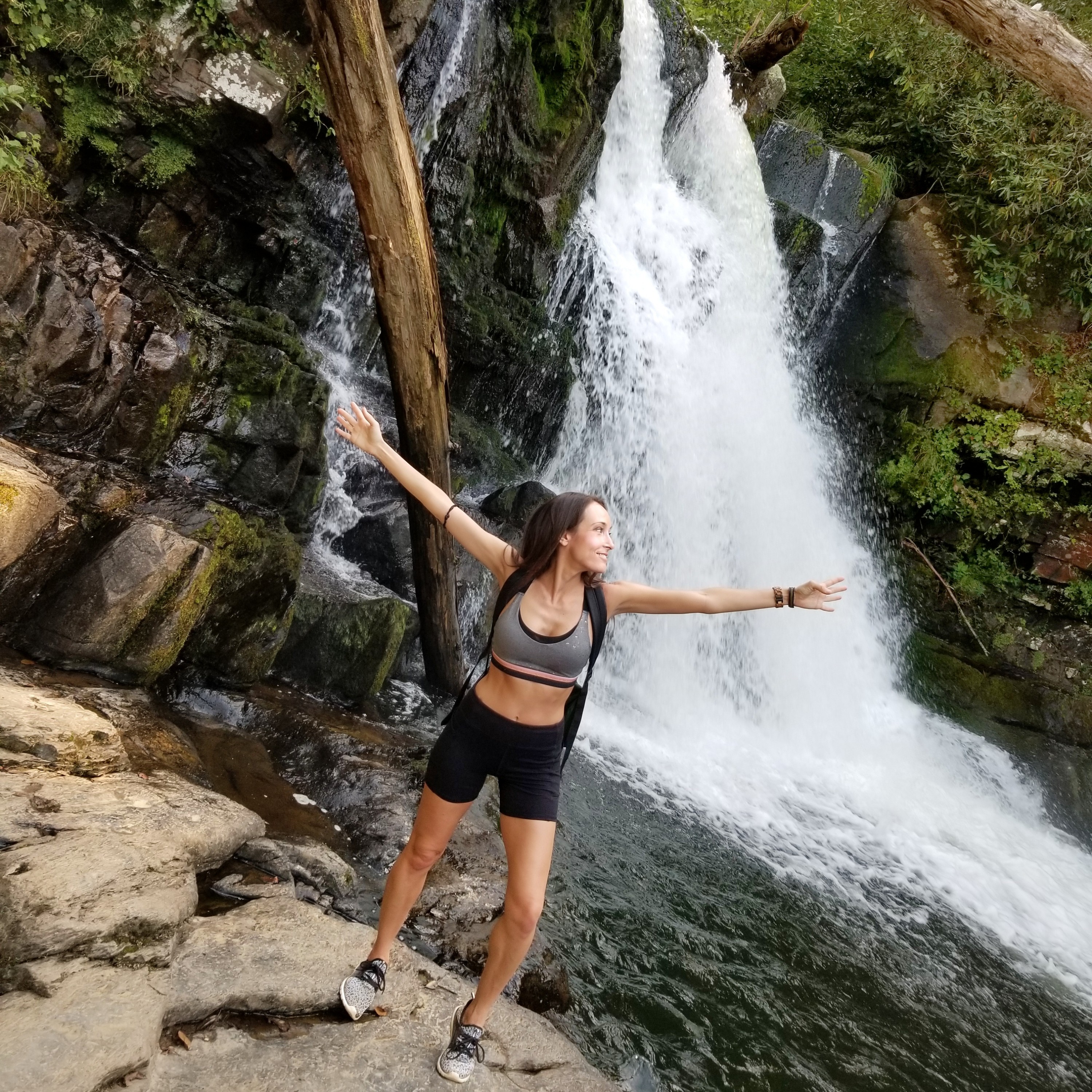 Woman with outstretched arms in front of a waterfall