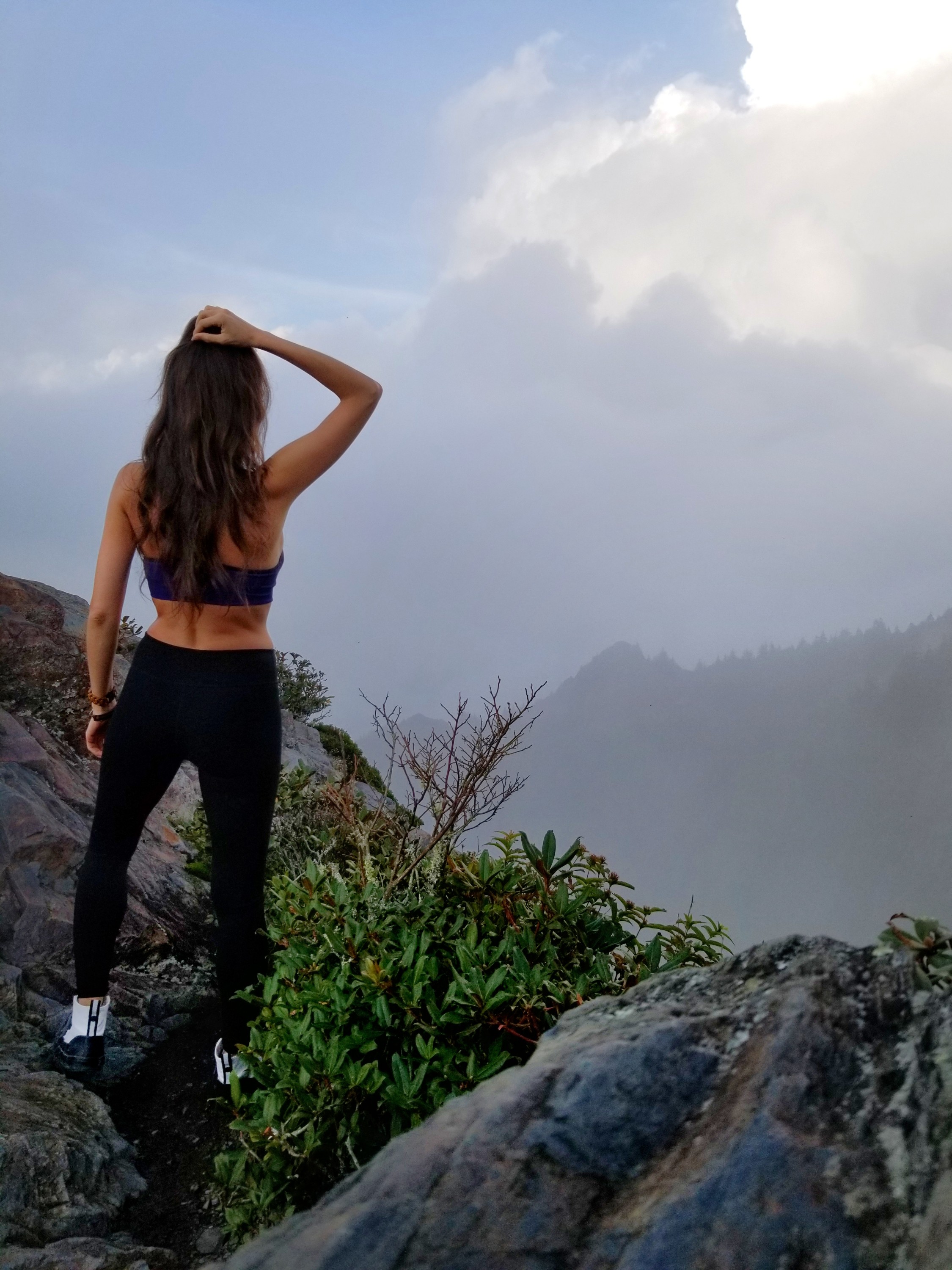 Woman standing on the edge of a mountain looking out over a foggy area