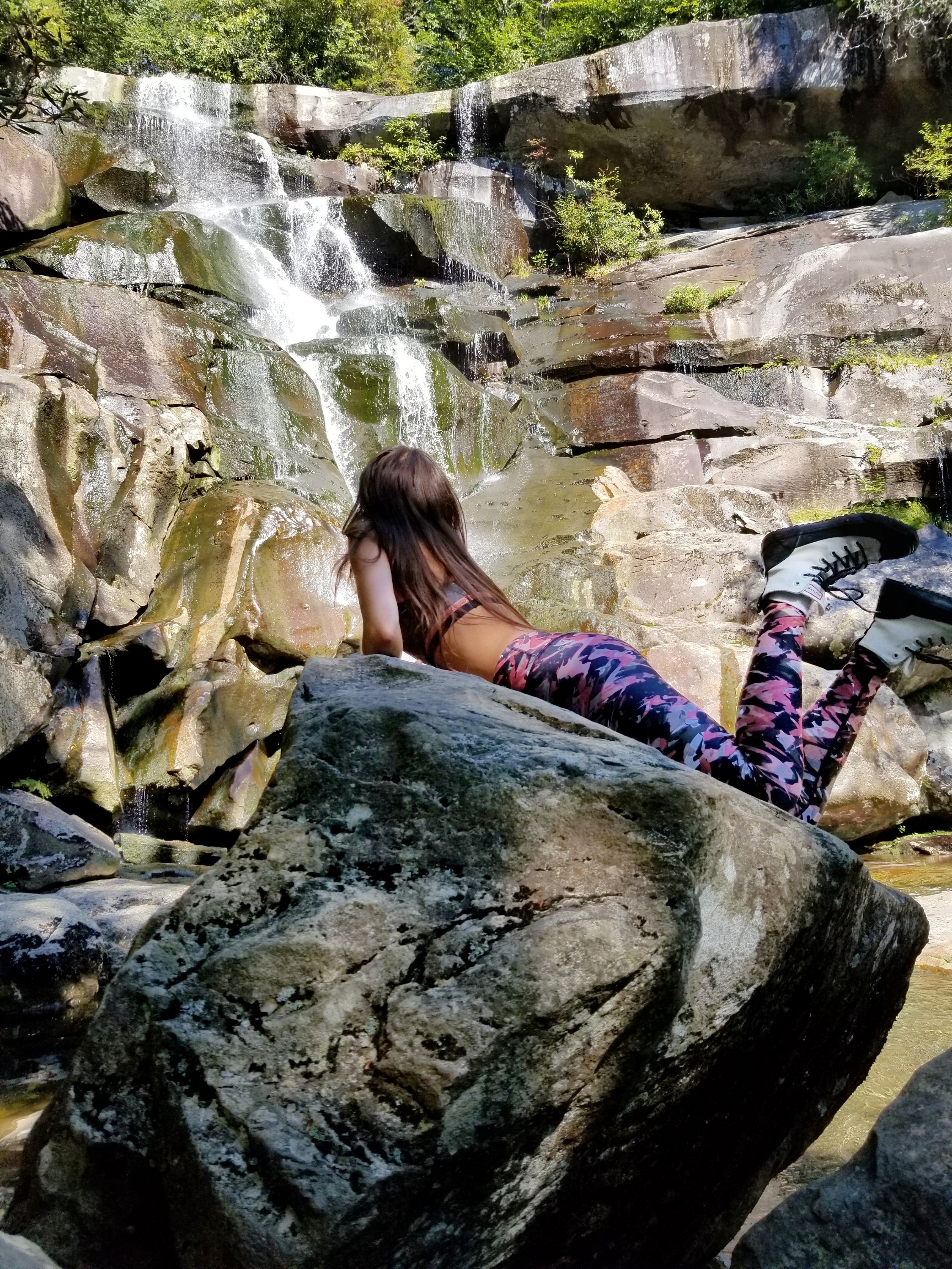 Woman laying on a rock and looking at a waterfall