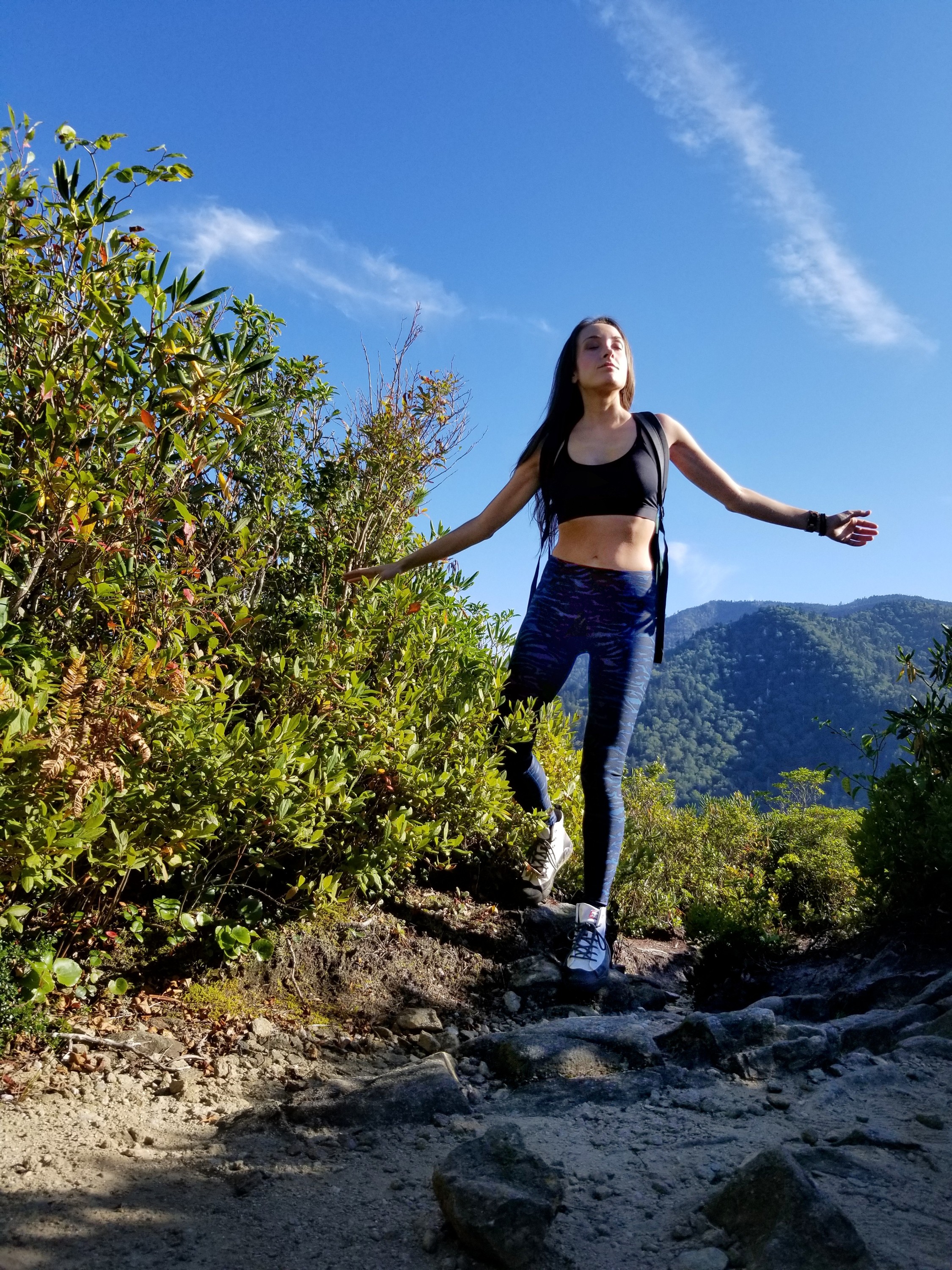 Woman with arms outstretched on a hiking path with mountains in the background
