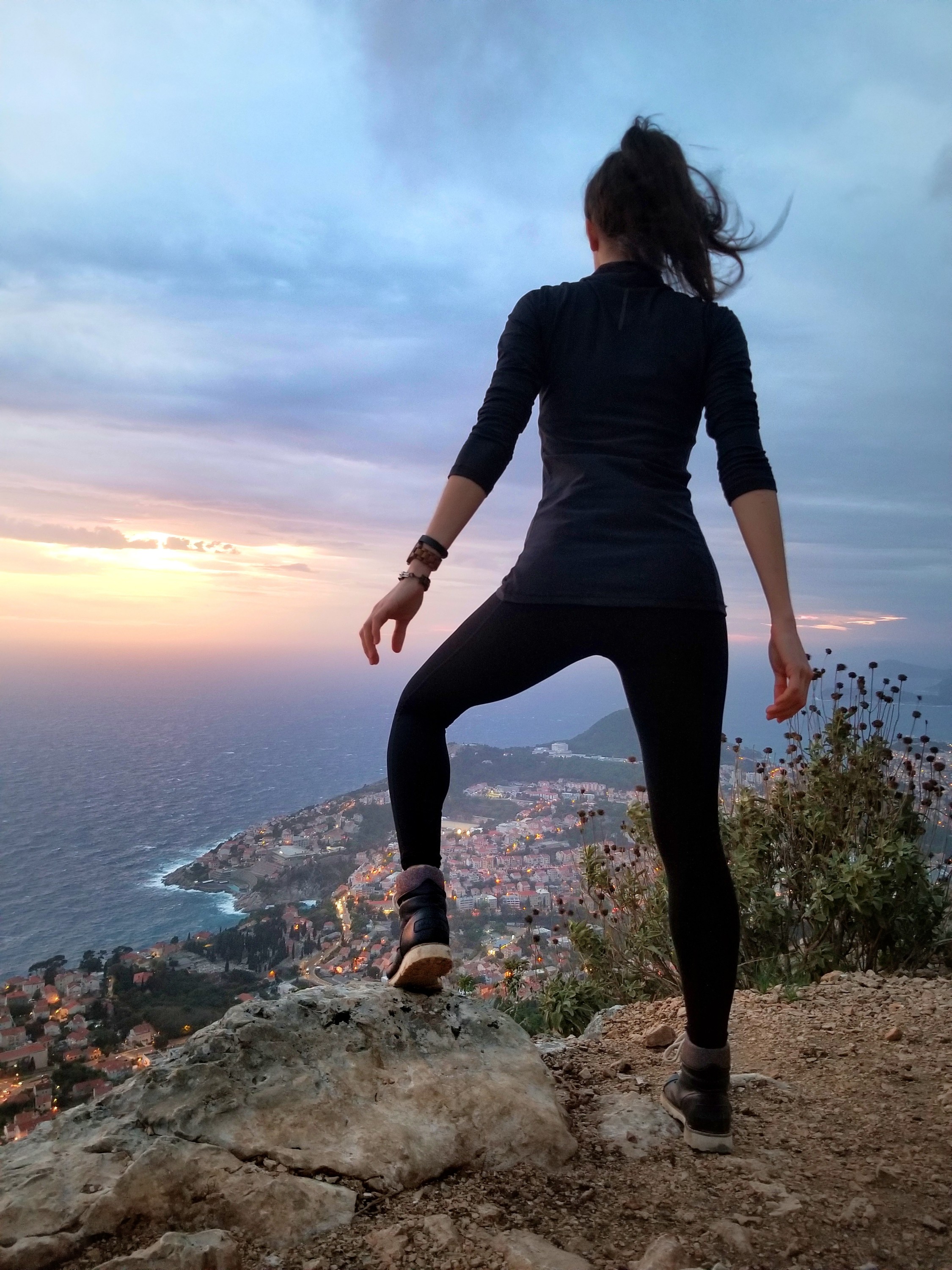 Woman standing on a cliff, overlooking a city on the coast of an ocean