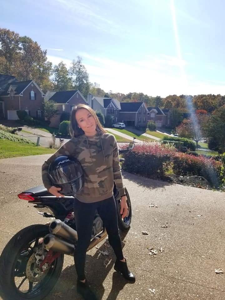 Woman holding a motorcycle helmet and standing next to a motorcycle