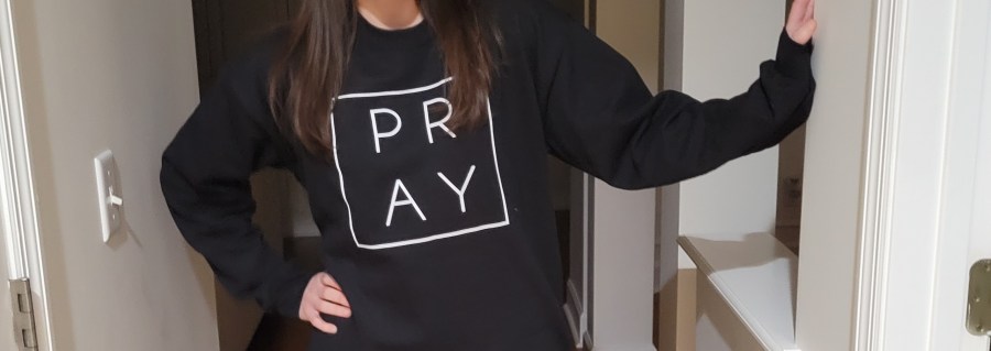 Woman wearing a black sweatshirt with the word PRAY on it