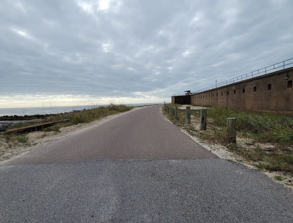 Paved road with water on one side and a brick wall on the other side