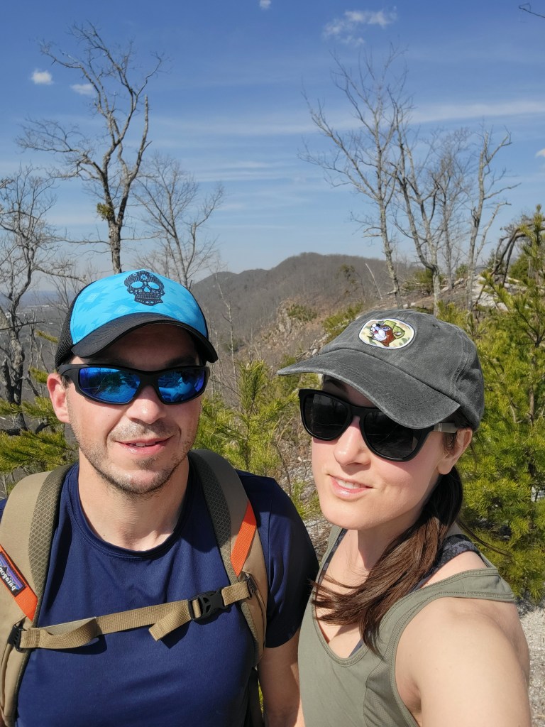Man and woman taking a selfie while hiking with a mountain view behind them
