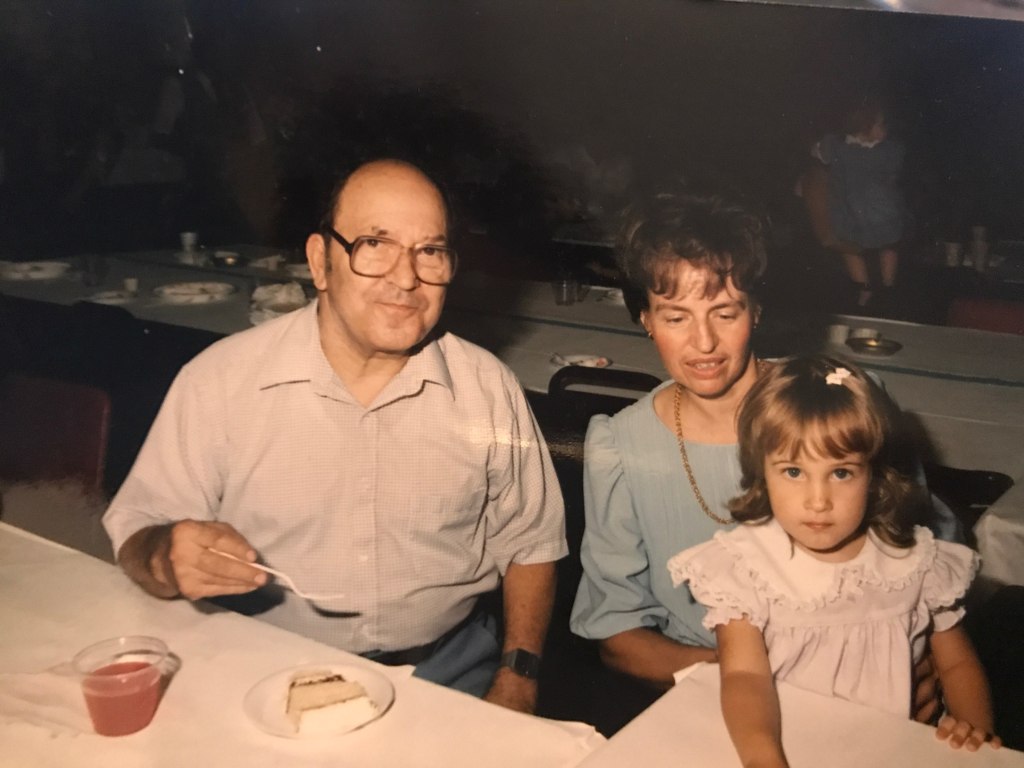 Older male and female couple eating cake with with toddler grandchild 