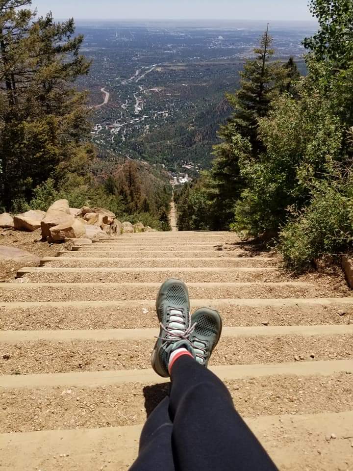 Feet crossed, wearing hiking boots at the top of a steep stone stairway in the mountains 