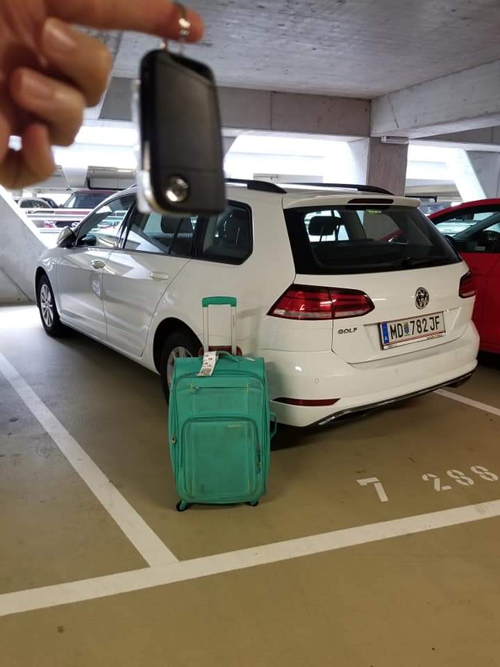 White hatchback Volkswagen in a parking garage with a green suitcase next to it