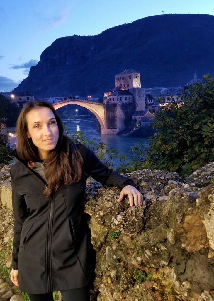 Woman in a black coat, posing with Stari Most bridge behind her, in Mostar, Bosnia and Herzegovina