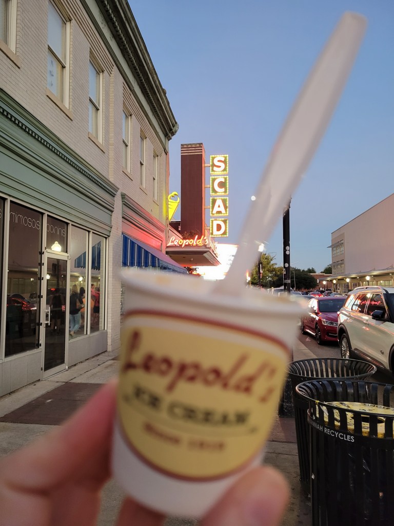 Cup of ice cream with spoon, held up for a photo with a neon sign at Leopold's in Savannah GA 