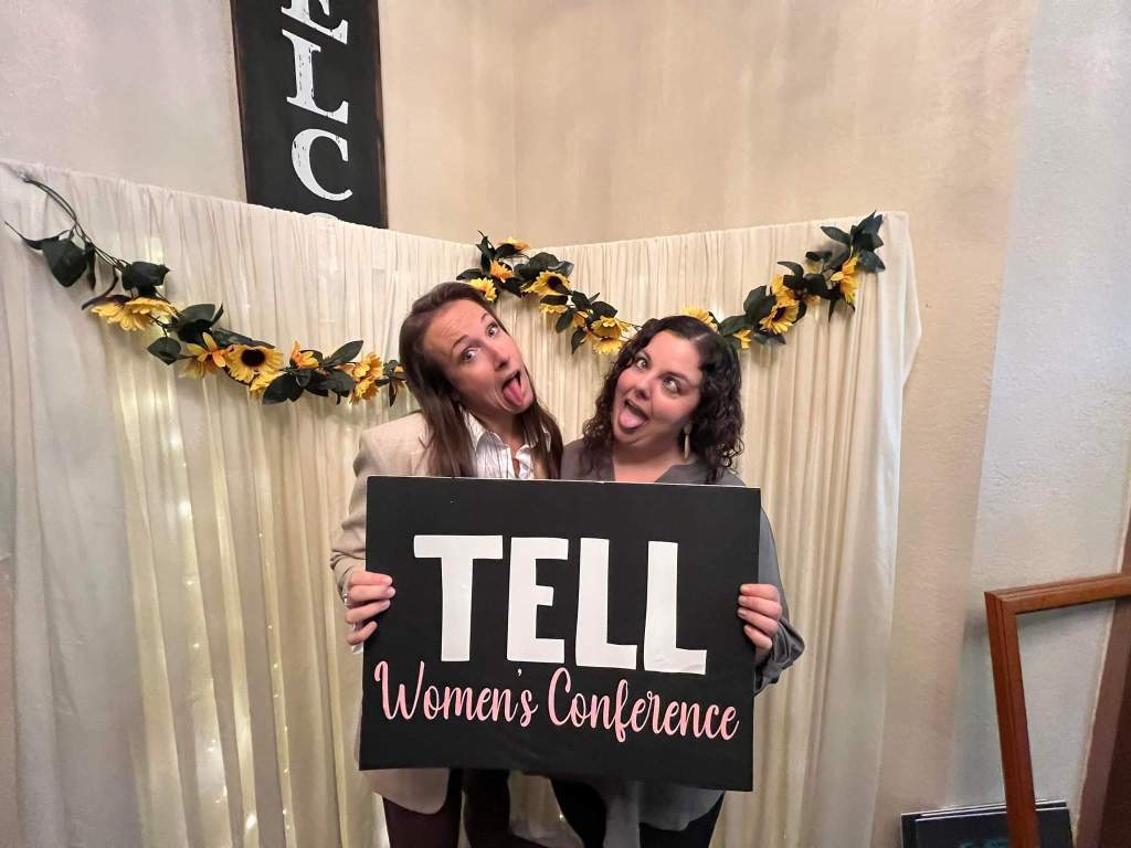 Two women posing with a sign that reads: "TELL Women's Conference"