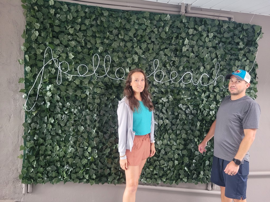 Woman and man standing in front of a wall with letters that spell "Apollo Beach"