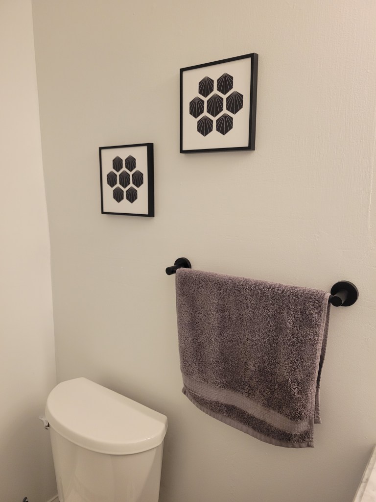 Bathroom with a toilet, towel holder, and two black and white square pieces of art work on the wall