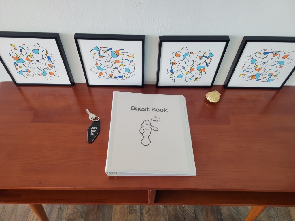 Four, square pieces of abstract art on a table with a "Guest book"