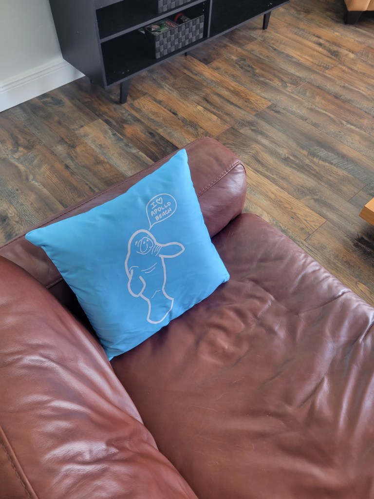 Blue pillow with a manatee on it, set on a brown leather couch