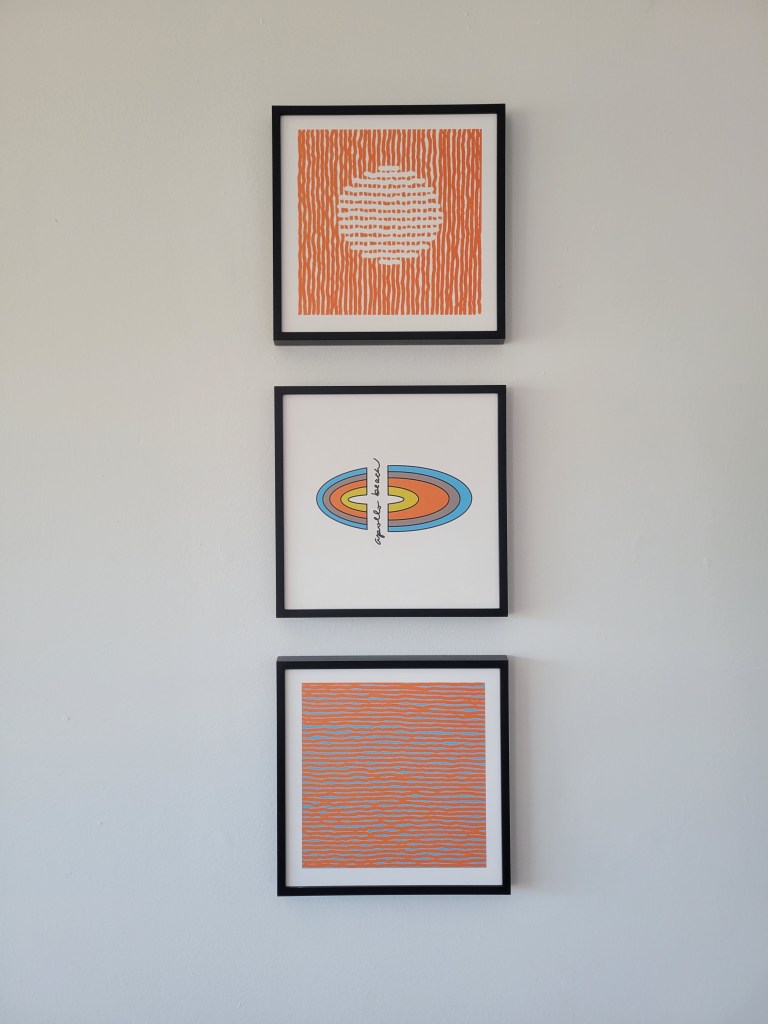 Three square abstract art pieces, hung in a vertical line