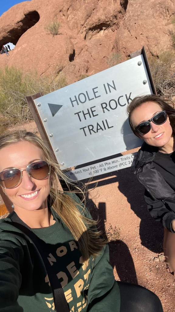 Two women posing near a sign for "Hole in the Rock"