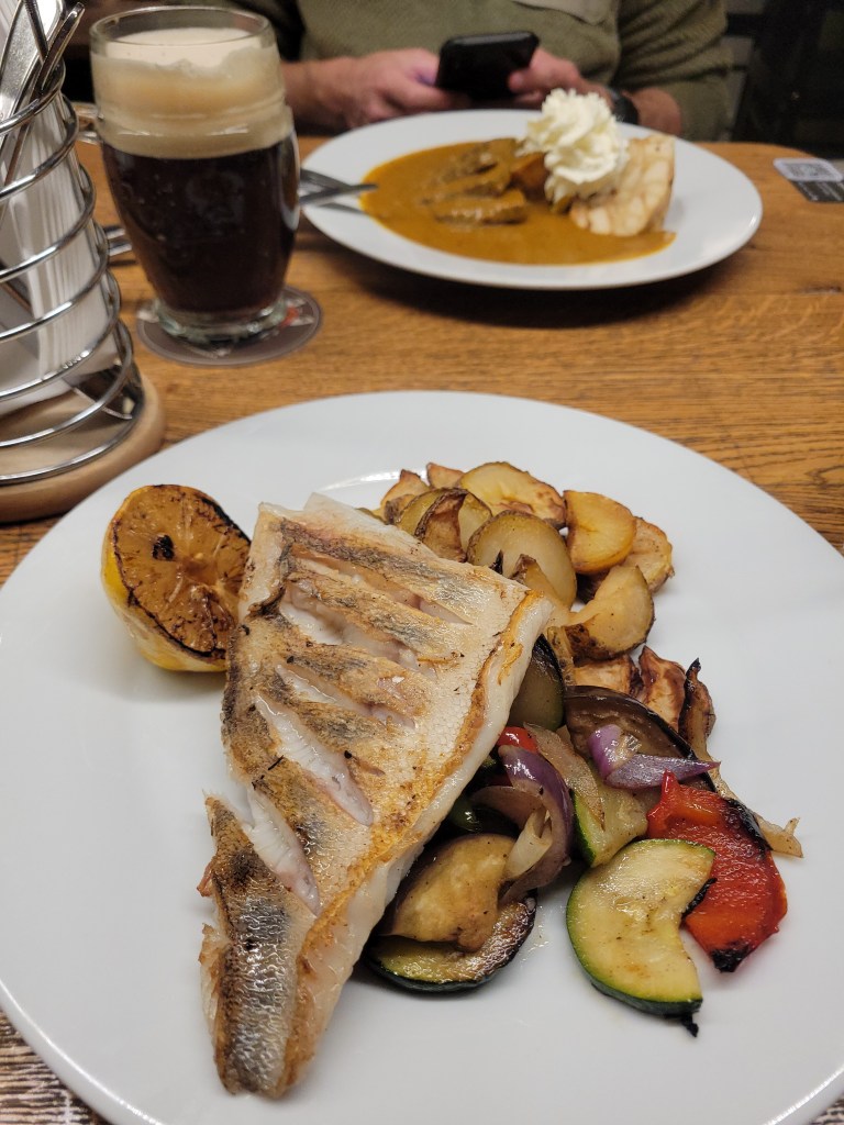 Plate of grilled fish, roasted potatoes and vegetables, and a second plate of meat and dumplings on a table in a restaurant 