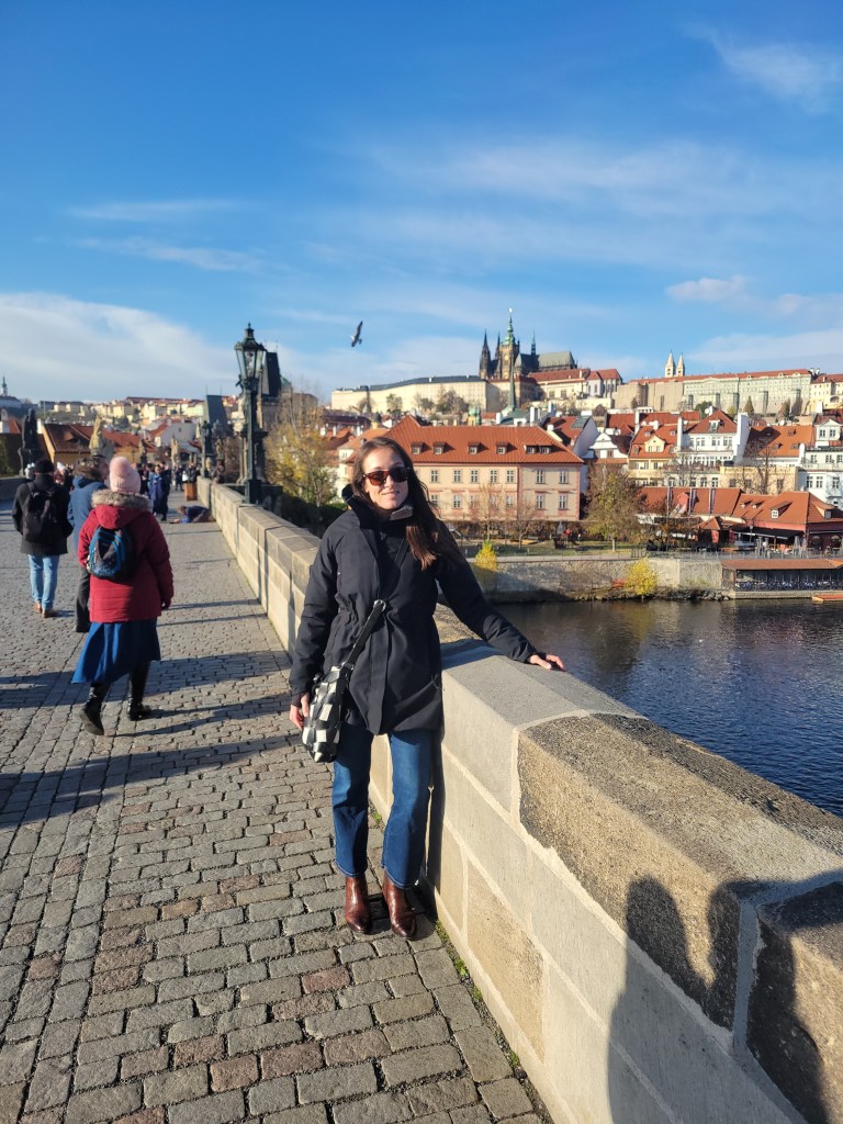 Woman on a cobblestone bridge in Prague with the city view in the background 