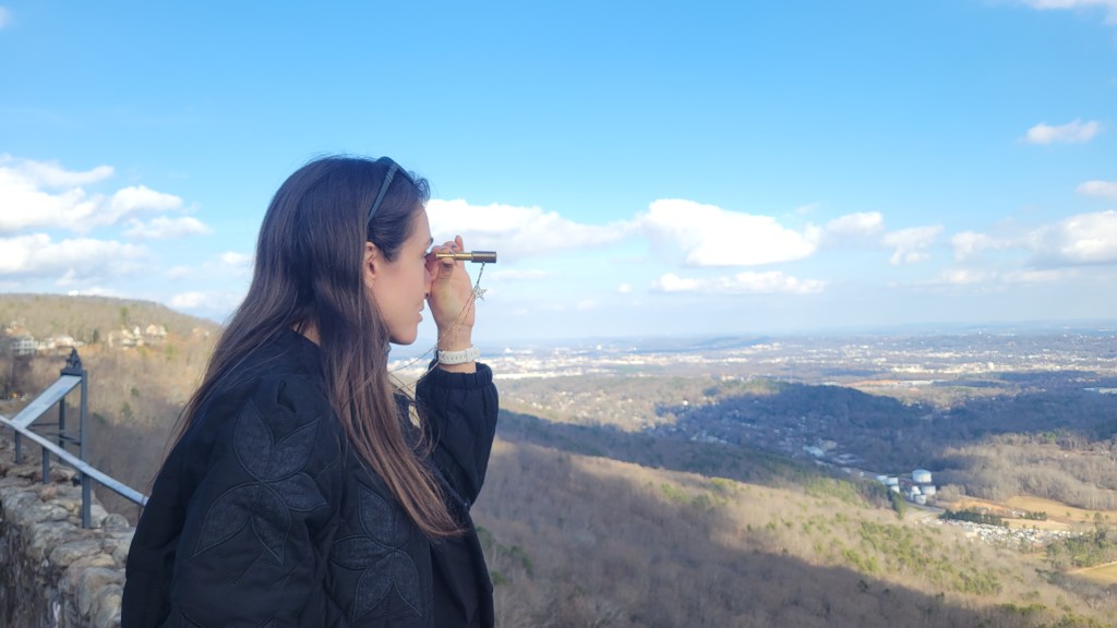 Woman looking in a small spyglass on a mountaintop