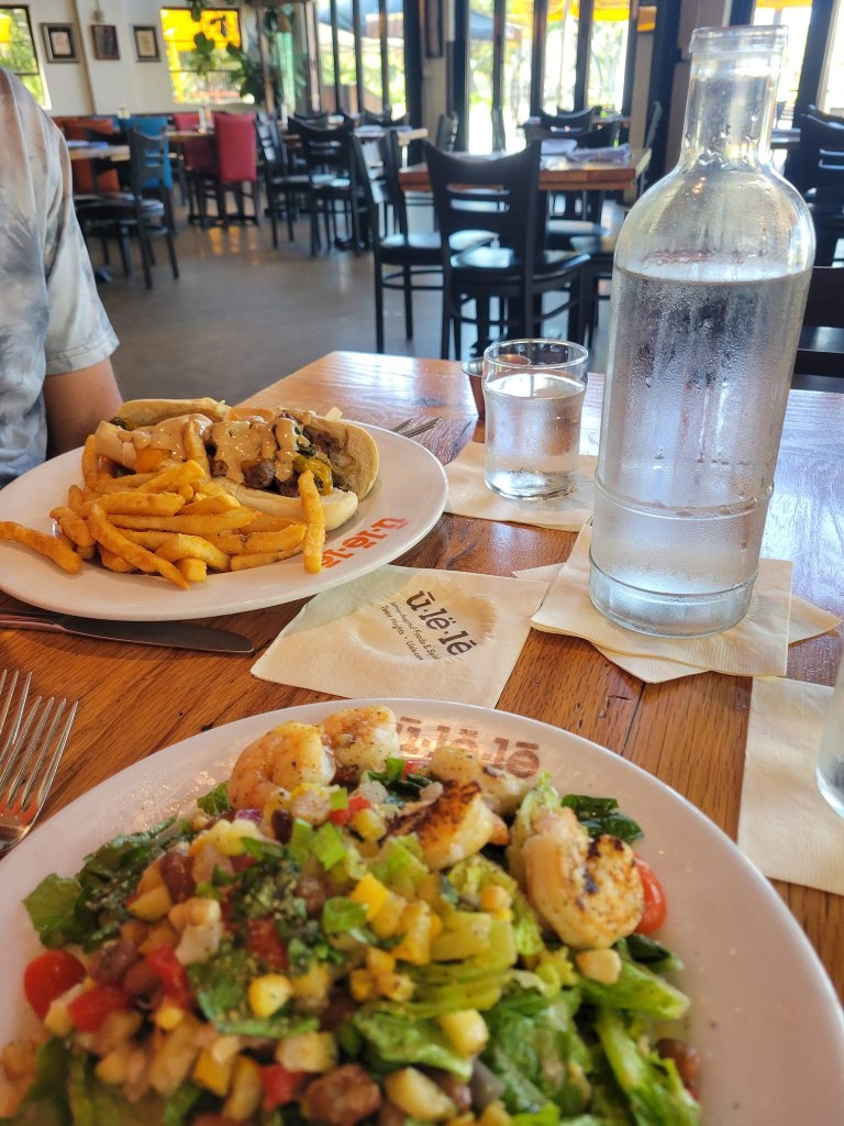 Shrimp salad, fries, and a hot dog on white plates at a restaurant