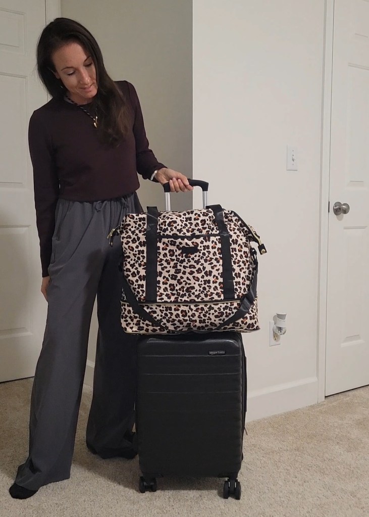 Woman standing next to a carry-on suitcase and large travel weekender tote bag